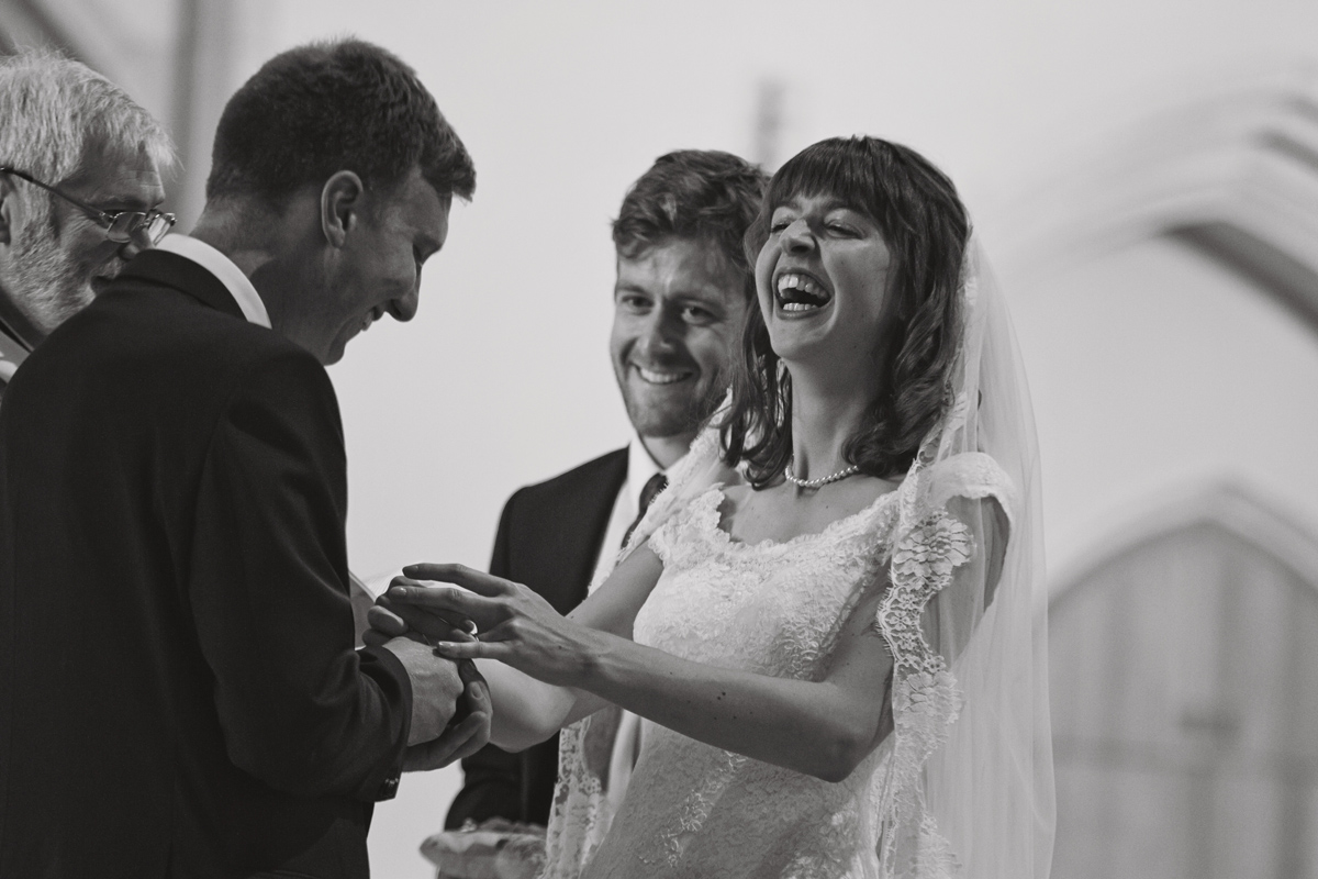 A black and white picture of the bride laughing as she receives her ring at a wedding
