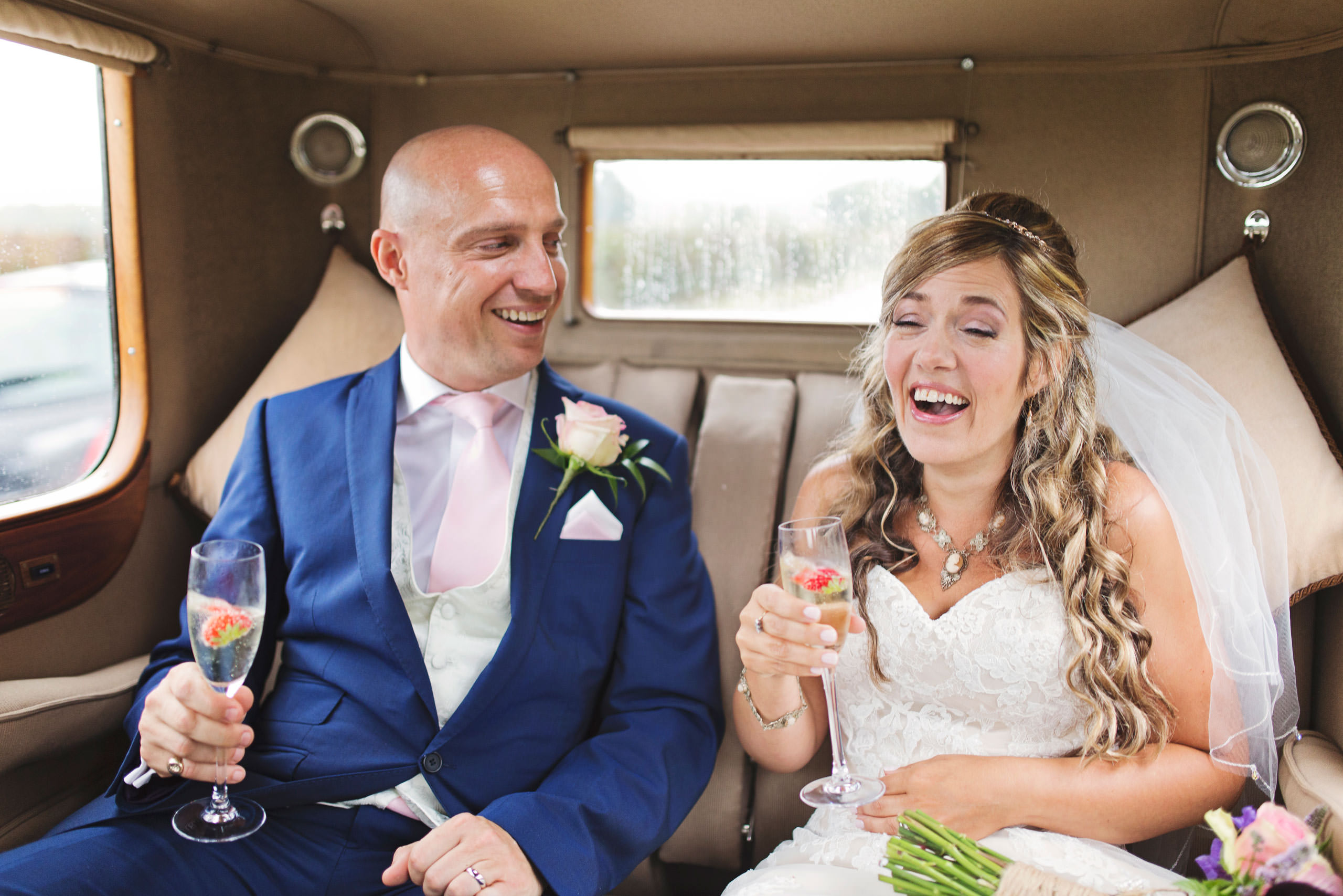 Newlyweds enjoy champagne in the back of a classic wedding car