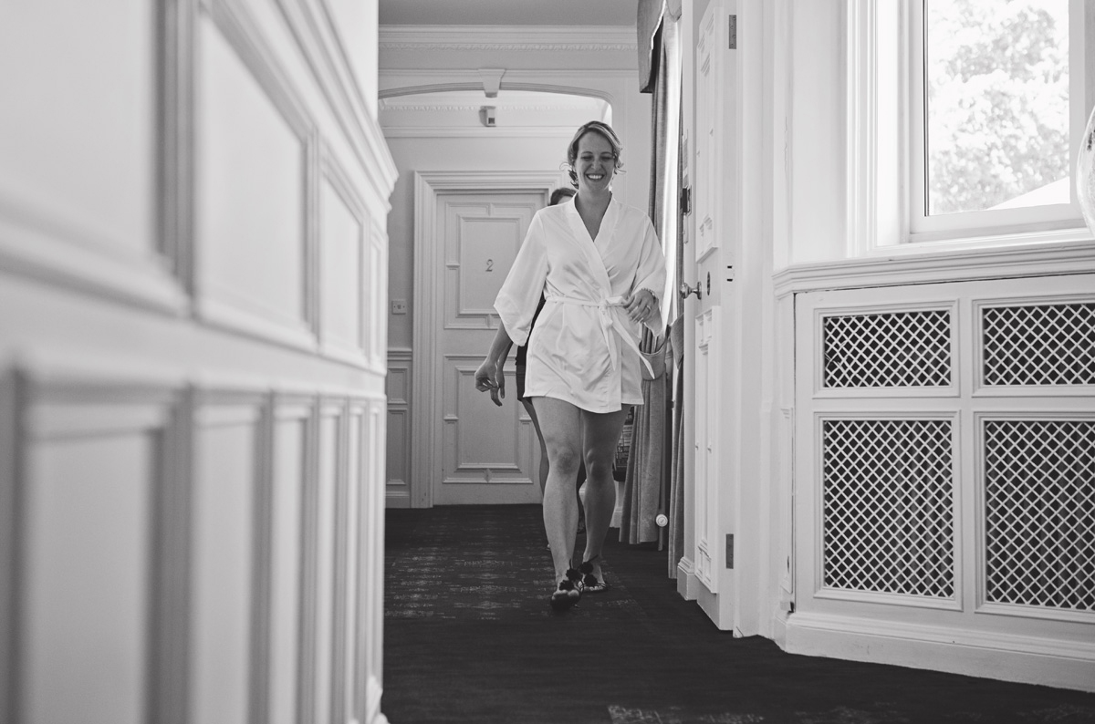 A smiling bride to be walking down a corridor in a towel robe