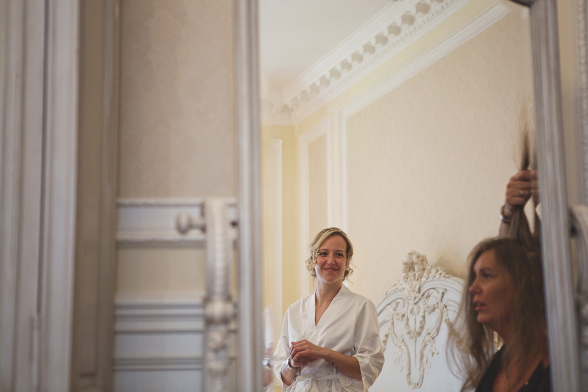 A woman watches her bridesmaid having her hair done on her wedding day