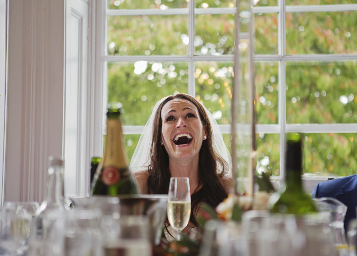 A bride bursts out laughing during the speeches at her wedding breakfast
