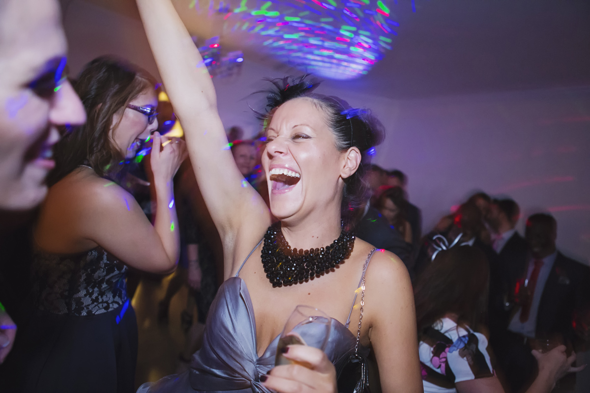 A wedding guest raise her hand and laughs while dancing at a reception