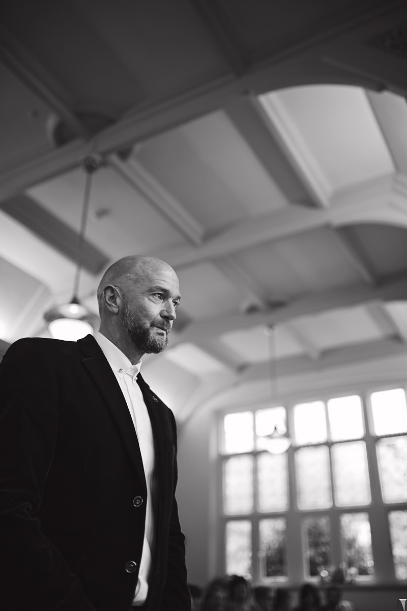 A low angle black & white shot of a pensive looking groom awaiting his bride at their wedding
