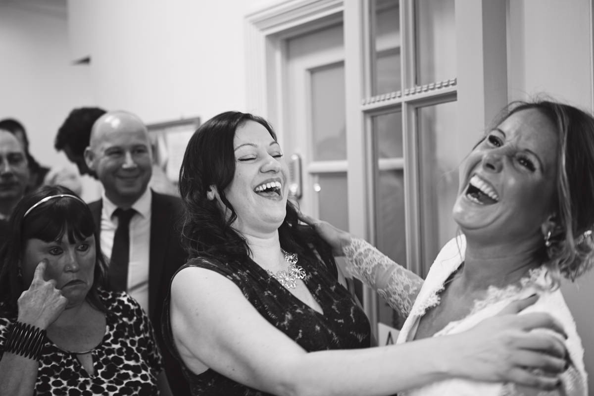 A bride bursts out laughing with a friend during the lineup at her wedding