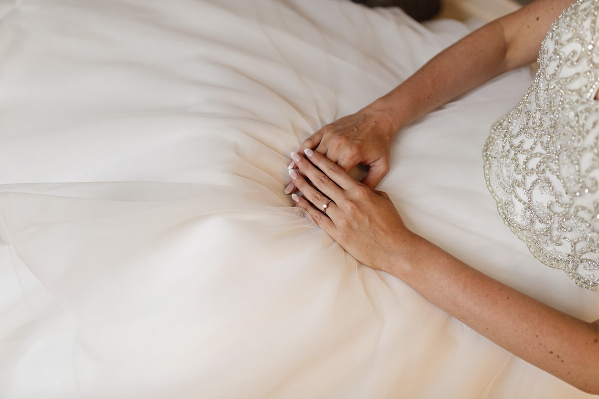 Close up of a bride's hands resting on her lap wearing a wedding dress