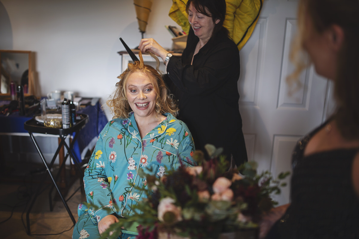 A bride to be looks at her bouquet while getting her hair styled