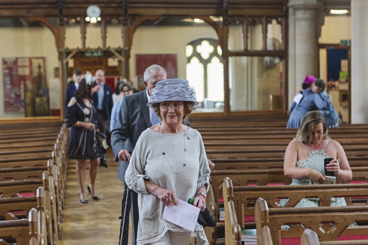 A female wedding guest in a blue hat takes her seat at the church