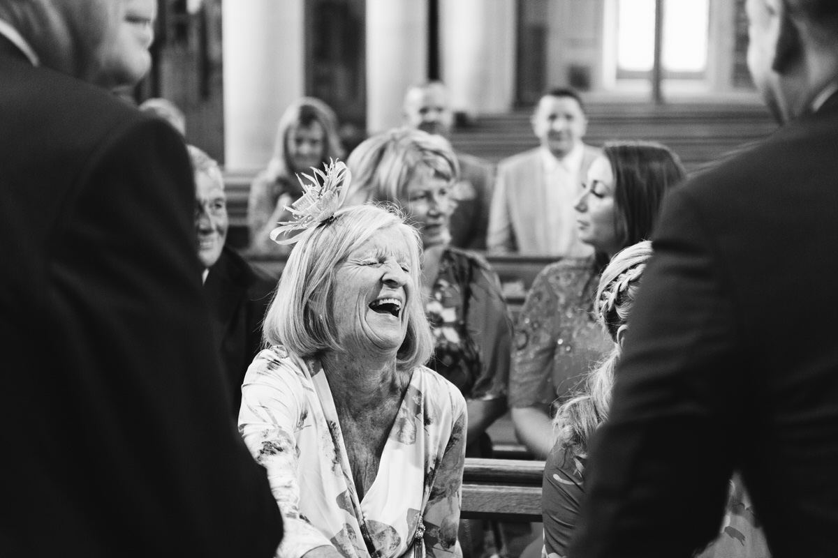 A black and white image of a wedding guest laughing in a church
