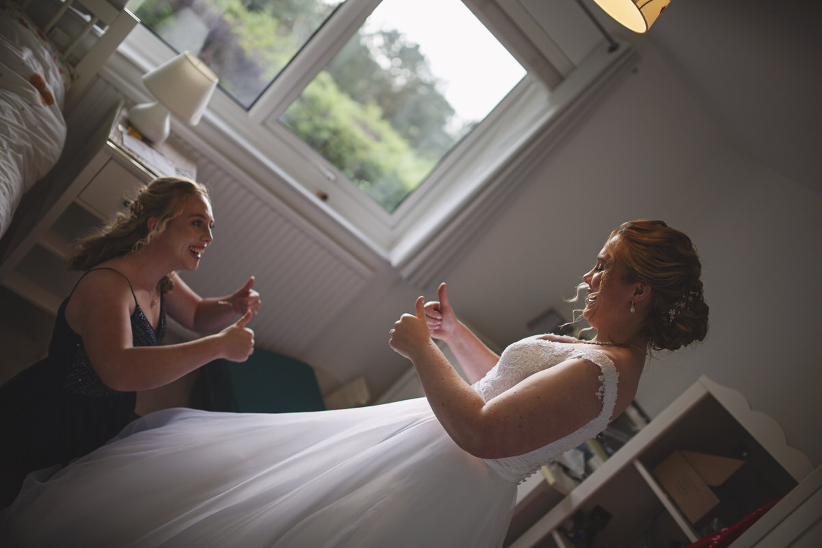 A bride and bridesmaid give each other the thumbs up before leaving for the church