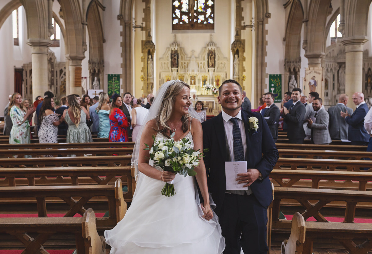 A smiling bride and groom walk down the aisle after getting married