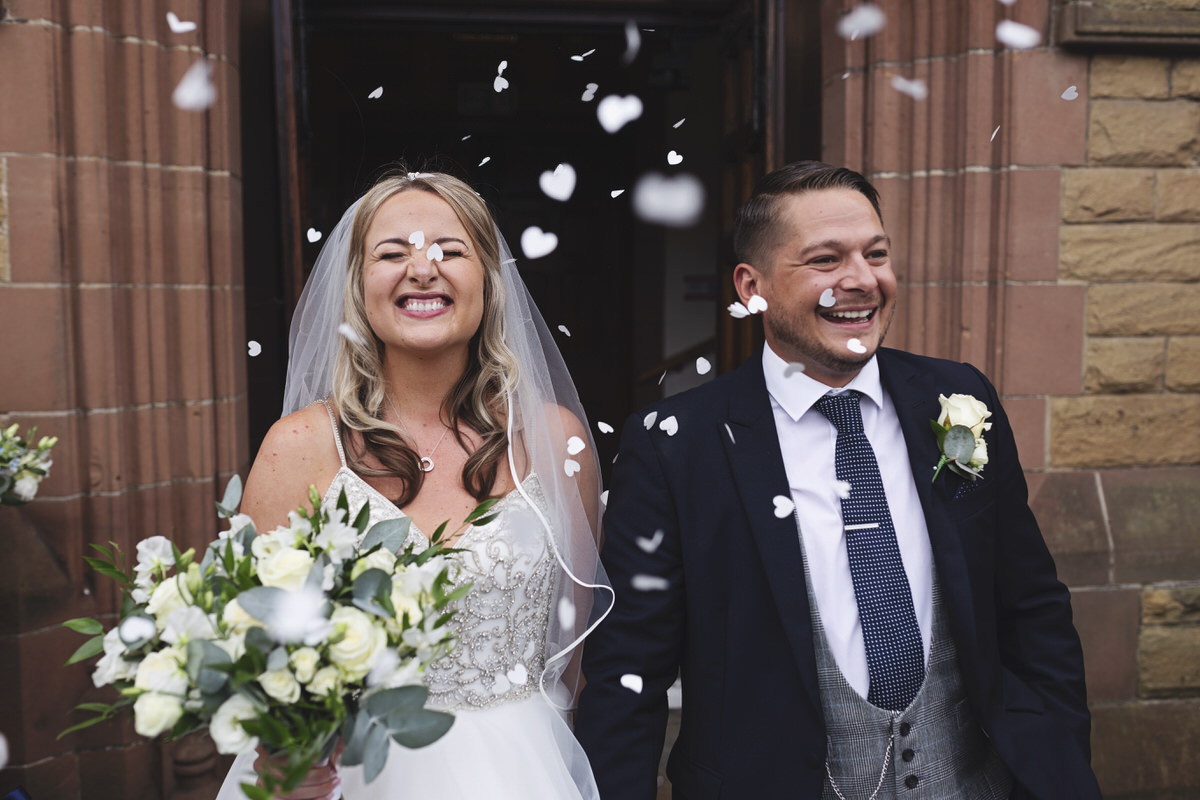 A bride and groom get covered in confetti after their wedding