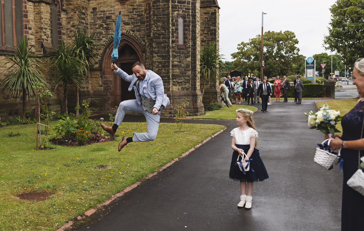A guest jumps for joy outside a church at a wedding