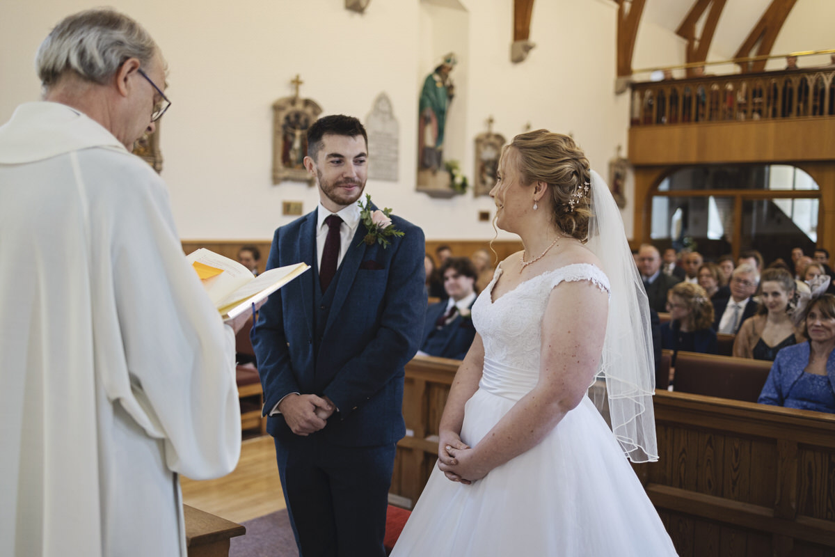 A bride and groom smile at each other at the alter of a church