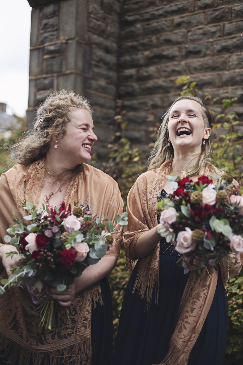 Two bridesmaids share a joke outside a church