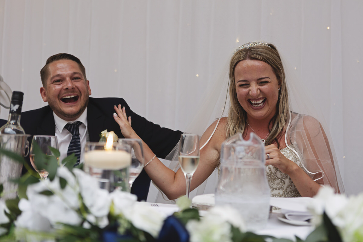 Newlyweds laughing at a best man's speech at a wedding reception