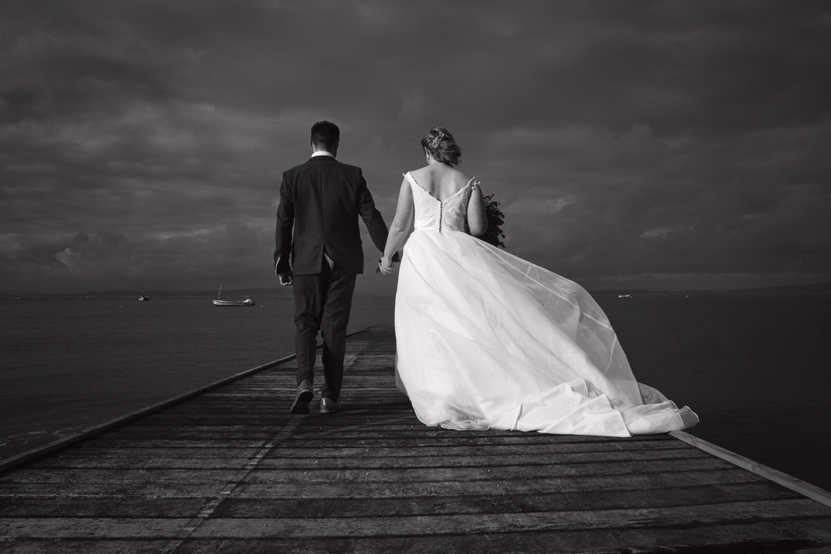 Newlyweds take a stroll along a jetty by the coast
